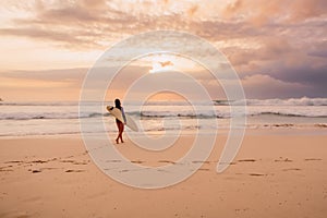 Surf girl go to ocean for surfing. Surfer woman on a beach at sunset