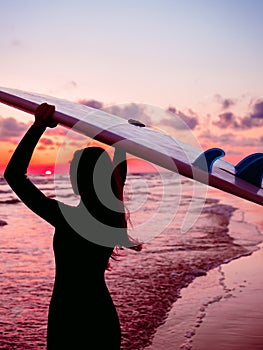 Surf girl with long hair go to surfing. Silhouette of a woman with surfboard on a beach at sunset or sunrise. Surfer and ocean