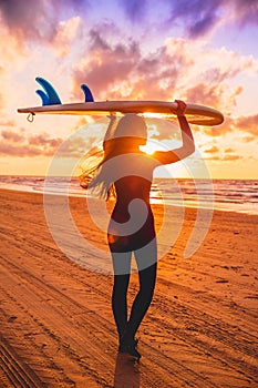 Surf girl with long hair go to surfing. Young woman with surfboard on a beach at sunset.