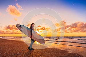 Surf girl with longboard go to surfing. Woman with surfboard on a beach at sunset.