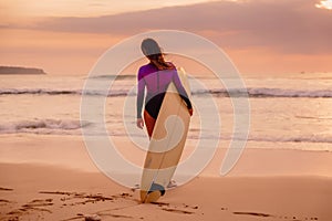 Surf girl with surfboard on a beach at sunset or sunrise