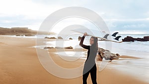 Surf lady going to surfing, woman with surfboard on beach by seaside looking and smiling at camera, panorama, copy space