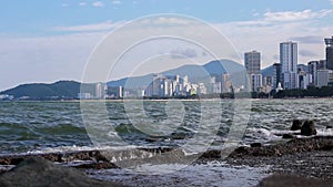 Surf overlooking city, calm waves, reinforced concrete fortifications on coastline.