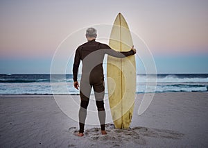 Surf, sea and sport with a man on the beach with his surfboard looking at the ocean view or horizon at sunset. Health