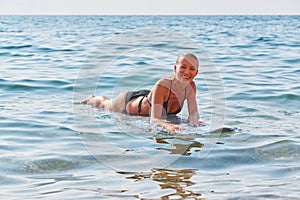 Surf sport, adventure trip and beach day concept. Happy lady floating on surfboard in ocean. Wavy sea on summer day.