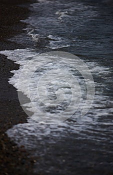 The surf wave line on a dark pebble beach in the evening