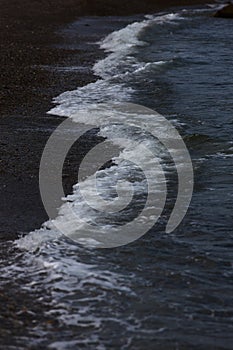 The surf wave line on a dark pebble beach in the evening