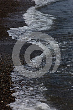 The surf wave line on a dark pebble beach in the evening