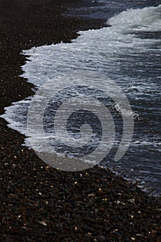 The surf wave line on a dark pebble beach in the evening