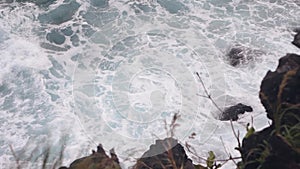 Surf waves breaking on the rocky shore forming seafoams.