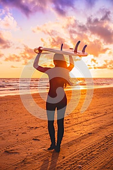 Surf woman with long hair go to surfing. Surfer with surfboard on a beach at sunset