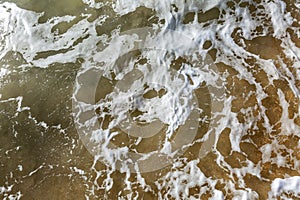 The surface of foamy sea water on a sandy shore. Background. Space for testing. Close-up