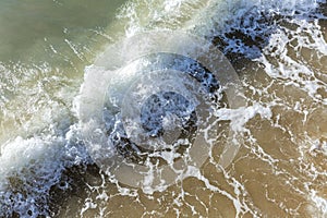 The surface of foamy sea water with a wave on the sandy shore. Background. Space for testing. Close-up