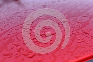 The surface and glass of the red car covered with raindrops