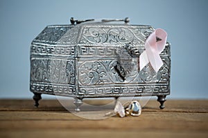 Surface level view of pink Breast Cancer Awareness ribbon with chest and rings on wooden table