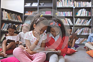 Surface level view of two relaxed schoolgirls looking at a digital tablet