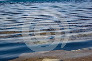 The surface is salty sea water, swaying in small waves near the shore, through the transparent bottom you can see stones