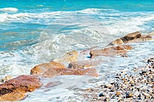 Surface of sea waves during windy summer day, sea shore with pebble stones and cutwater.