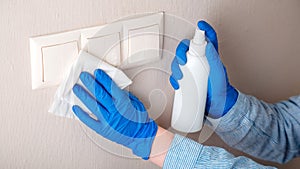 Surfaces disinfection. Houseworker in rubber blue gloves clean light switch with cloth on wall by alcohol spray and rag. New