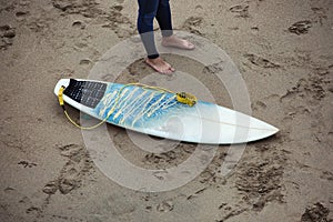 Surfboard on the beach next to the surfer legs.