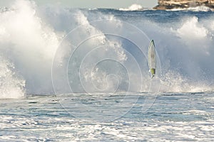 Surfboard flying in front of breaking wave