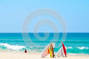 Surfboard on sand tropical beach with sea wave and blue sky background.