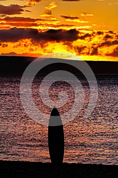 Surfboard standing upright on the beach at sunset on Maui.