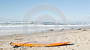 Surfboard for surfing lying on beach sand, California coast, USA. Ocean waves.