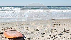 Surfboard for surfing lying on beach sand, California coast, USA. Ocean waves.