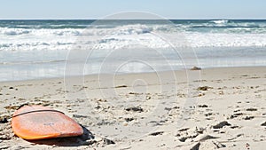 Surfboard for surfing lying on beach sand, California coast, USA. Ocean waves.