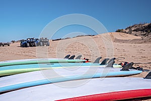 Surfboards laying on sand with vehicle at beach against blue sky