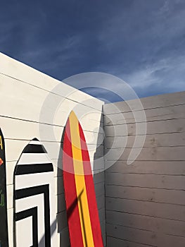 surfboards standing near the wall of white planks against the sky