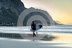 A surfer on Betty`s Bay beach at sunset in the Western Cape, South Africa