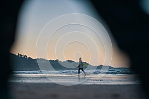 Surfer boy walking on the beach after sunset