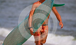 Surfer carrying his surboard on the shore of the beach