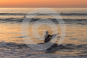 Surfer carrying the surfboard into water with waves in the sunset