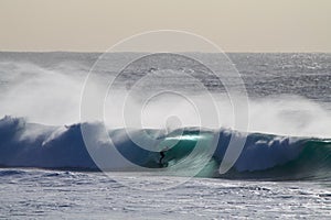 Surfer entering a huge blue barrel in the sea under a clear sky at daytime