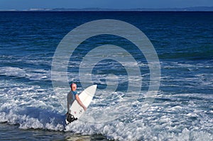 Surfer entering the ocean with his board