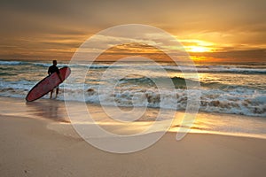 Surfer entering the ocean at sunrise