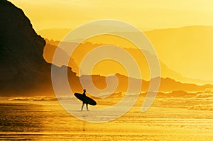 Surfer entering water at misty sunset