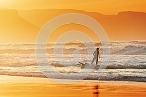 Surfer exiting water at sunset