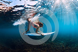 Surfer girl in bikini with surfboard dive underwater with under barrel ocean wave