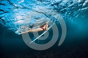 Surfer girl in bikini with surfboard dive underwater and wave