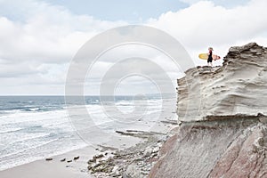 Surfer girl on cliff near ocean