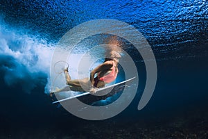 Surfer girl dive with surfboard under wave in transparent Pacific ocean