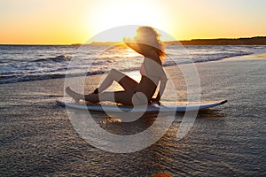 Surfer girl on her board at sunset