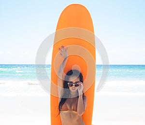 Surfer girl posing with her surfboard on the beach