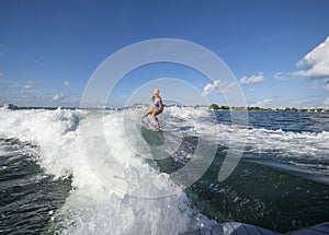 Surfer girl rides wave behind turbulent wave filled with white foam