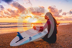 Surfer girl on sand beach with surfboard at warm sunset or sunrise.