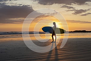 Surfer girl silhouette. Surf woman walking with surfboard on the beach.